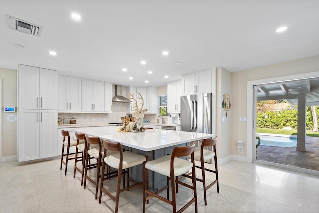 kitchen with white cabinetry, wall chimney exhaust hood, backsplash, a breakfast bar, and a kitchen island