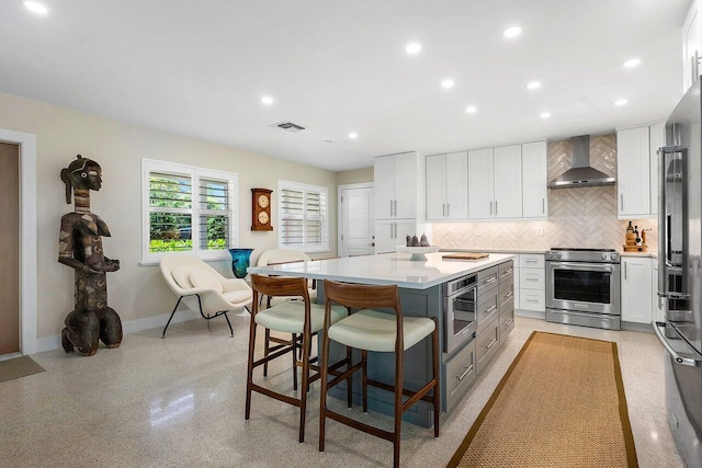 kitchen featuring white cabinetry, a center island, wall chimney range hood, and appliances with stainless steel finishes