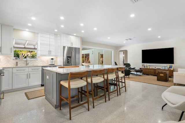 kitchen with appliances with stainless steel finishes, a kitchen breakfast bar, backsplash, white cabinets, and a center island