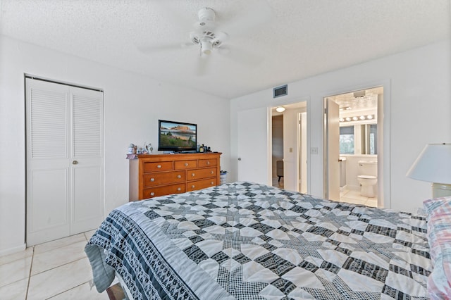 bedroom with a textured ceiling, ensuite bath, light tile patterned floors, a closet, and ceiling fan