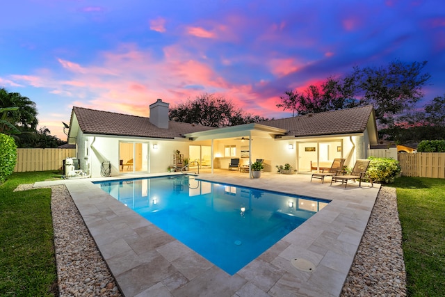 pool at dusk with ceiling fan and a patio