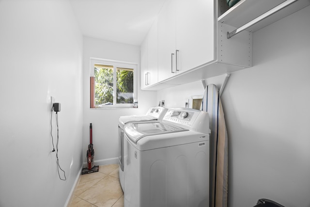 washroom featuring washing machine and dryer, light tile patterned floors, cabinet space, and baseboards