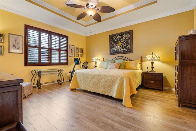 bedroom featuring light wood-type flooring, a tray ceiling, ceiling fan, and crown molding