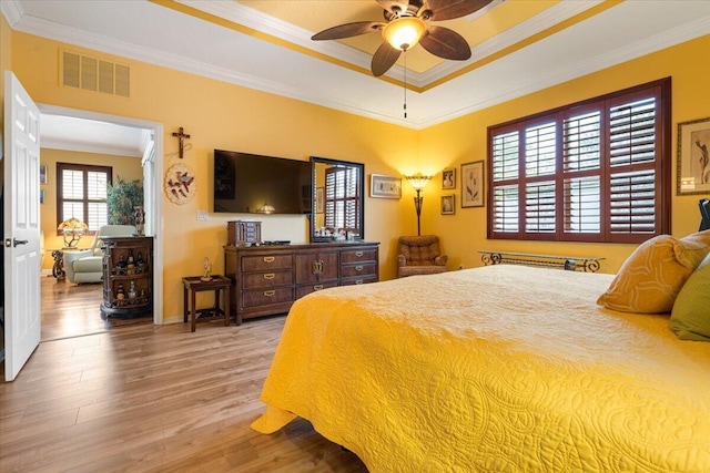 bedroom featuring light wood-type flooring, a tray ceiling, ceiling fan, and ornamental molding