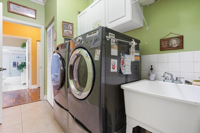 laundry area with washer and clothes dryer, cabinets, sink, light tile patterned floors, and ornamental molding