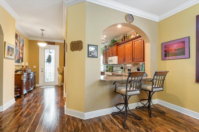 kitchen featuring white appliances, dark hardwood / wood-style floors, ornamental molding, light stone counters, and kitchen peninsula