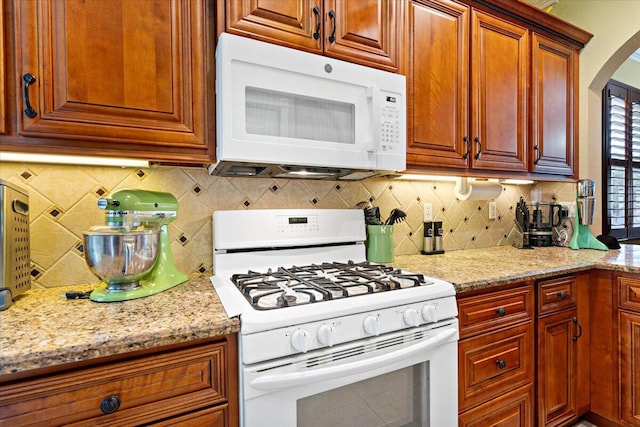 kitchen with tasteful backsplash, light stone countertops, and white appliances