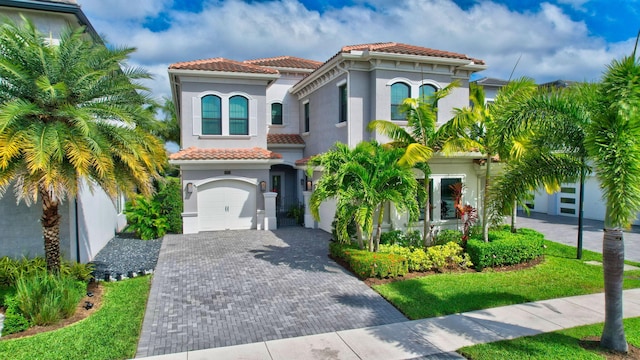 mediterranean / spanish home with a garage, decorative driveway, a tiled roof, and stucco siding