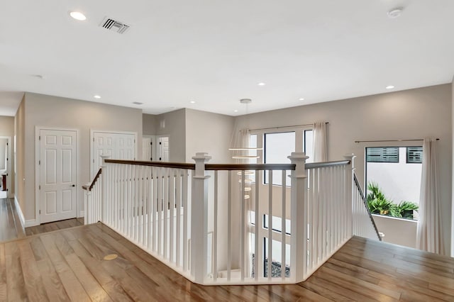 hall featuring recessed lighting, visible vents, light wood-style flooring, and an upstairs landing