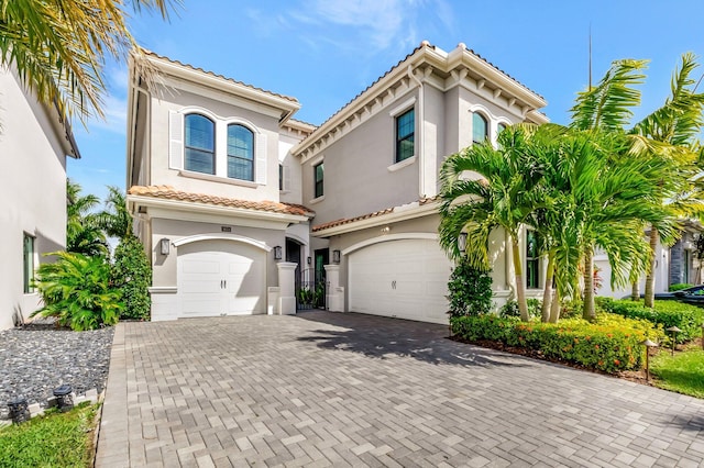 mediterranean / spanish house with a garage, a tile roof, and stucco siding