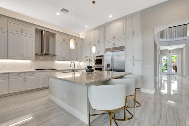 kitchen featuring appliances with stainless steel finishes, a sink, wall chimney range hood, and an island with sink