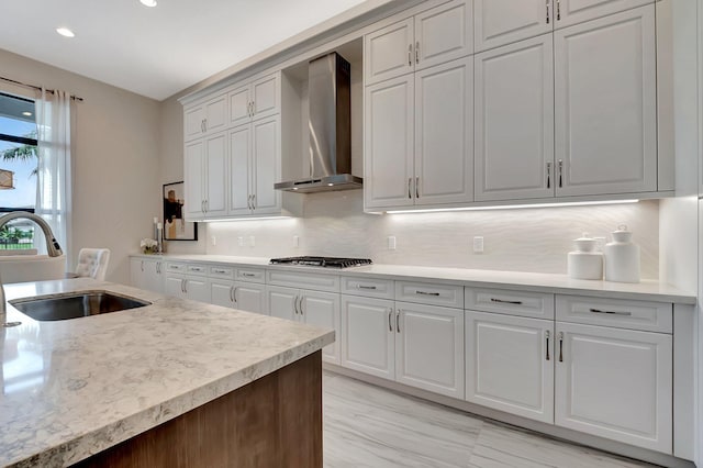 kitchen featuring stainless steel gas cooktop, wall chimney exhaust hood, a sink, white cabinetry, and backsplash