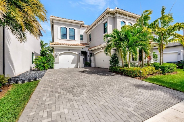 mediterranean / spanish home with decorative driveway, a tile roof, an attached garage, and stucco siding