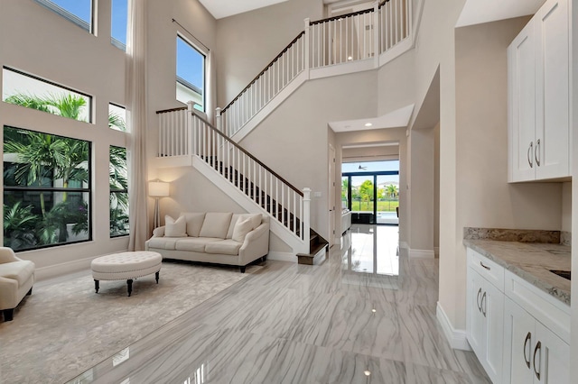 living area featuring stairs, marble finish floor, a towering ceiling, and baseboards