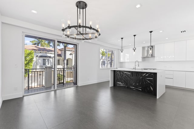 kitchen with white cabinets, a center island with sink, wall chimney range hood, and hanging light fixtures