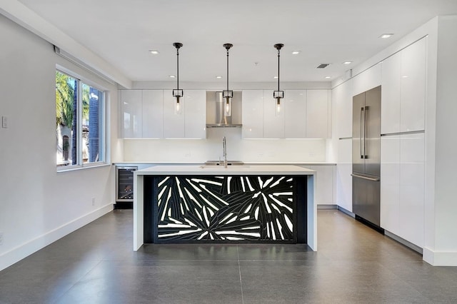 kitchen featuring white cabinets, a center island with sink, sink, wall chimney exhaust hood, and decorative light fixtures