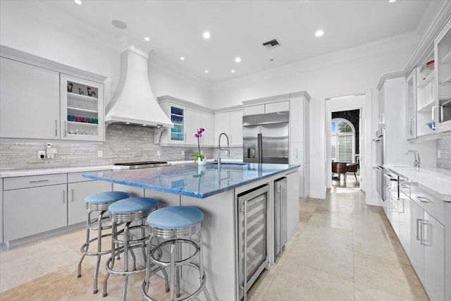 kitchen featuring a kitchen breakfast bar, custom exhaust hood, stainless steel appliances, a kitchen island with sink, and sink