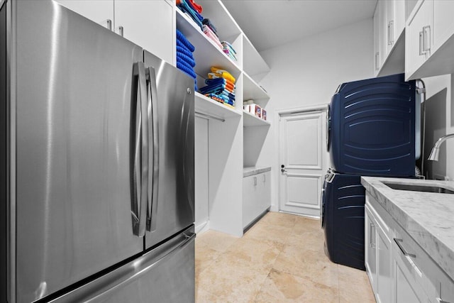 kitchen with stacked washer / dryer, stainless steel fridge, white cabinetry, and sink