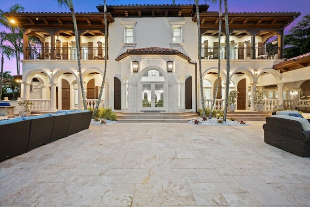 back house at dusk with a balcony, a patio, and french doors