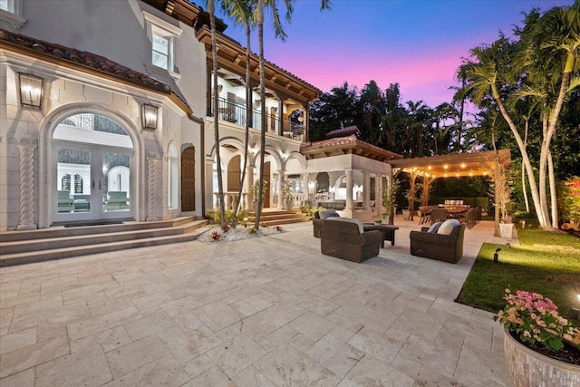 patio terrace at dusk with french doors, a pergola, a balcony, and an outdoor hangout area