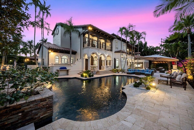 back house at dusk featuring an outdoor hangout area, a balcony, and a patio area