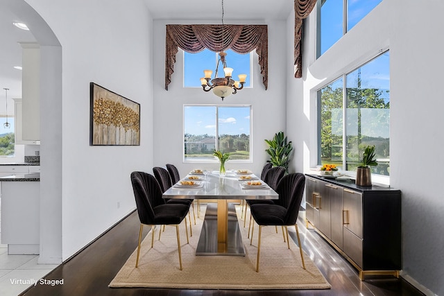 dining area featuring wood-type flooring, plenty of natural light, a towering ceiling, and an inviting chandelier