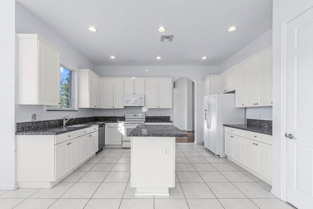 kitchen featuring light tile patterned floors, a kitchen island, dark stone counters, white appliances, and white cabinets