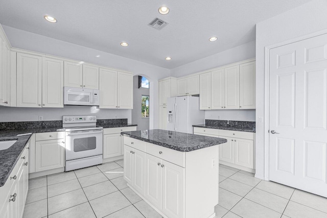 kitchen with white cabinets, a center island, white appliances, and dark stone counters