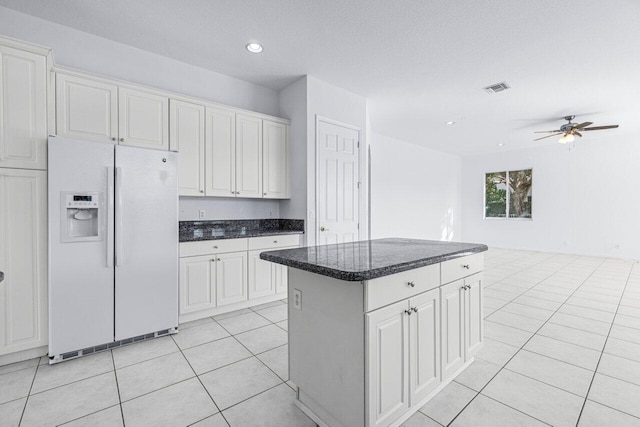 kitchen featuring light tile patterned floors, white cabinetry, white fridge with ice dispenser, and a kitchen island