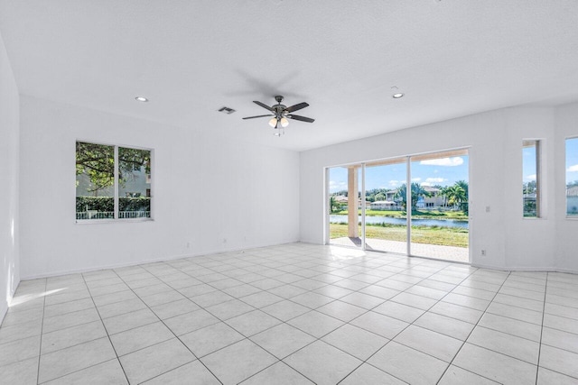 tiled empty room featuring ceiling fan, a water view, and a textured ceiling