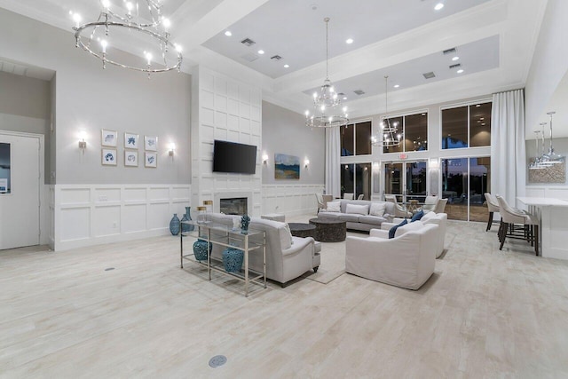 living room featuring light wood-type flooring, a large fireplace, a chandelier, and a towering ceiling