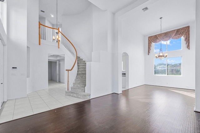 unfurnished living room featuring light hardwood / wood-style floors, a high ceiling, and an inviting chandelier