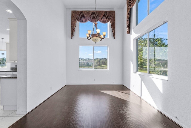 unfurnished dining area with hardwood / wood-style floors, a high ceiling, and an inviting chandelier