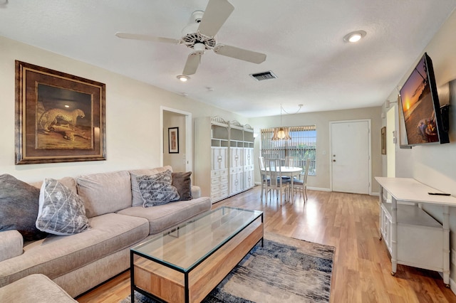 living room with light hardwood / wood-style floors and ceiling fan with notable chandelier