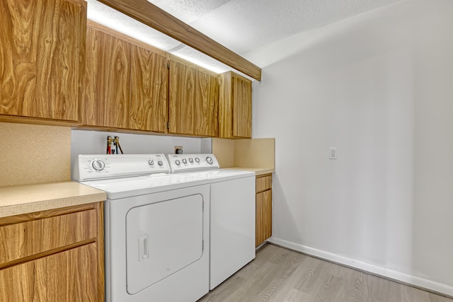 laundry area with washer and clothes dryer, cabinets, a textured ceiling, and light wood-type flooring