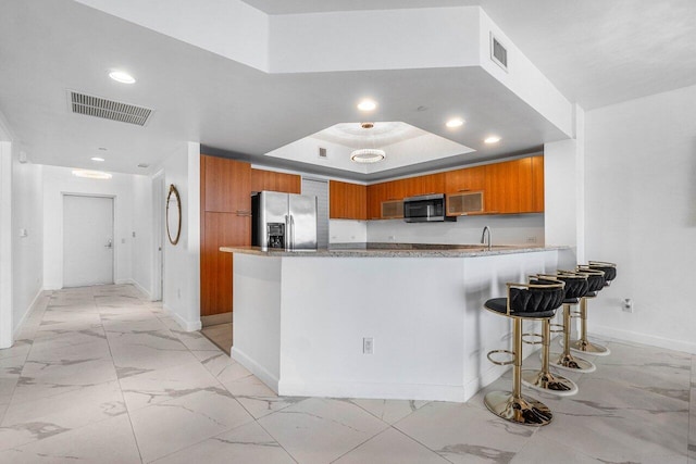 kitchen with kitchen peninsula, a kitchen breakfast bar, stainless steel appliances, a tray ceiling, and sink