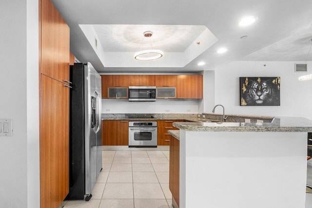 kitchen featuring stainless steel appliances, a raised ceiling, light stone counters, kitchen peninsula, and light tile patterned floors