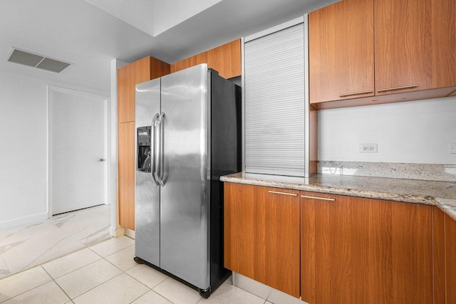 kitchen featuring stainless steel fridge with ice dispenser, light tile patterned floors, and light stone counters