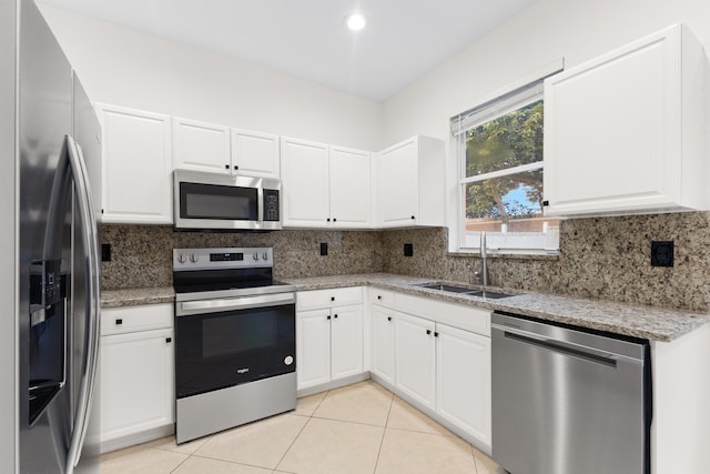 kitchen with light stone countertops, stainless steel appliances, sink, white cabinetry, and light tile patterned flooring