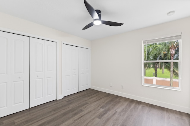 unfurnished bedroom featuring dark hardwood / wood-style flooring, two closets, and ceiling fan