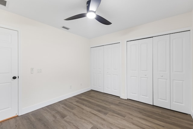 unfurnished bedroom with ceiling fan, dark wood-type flooring, and two closets