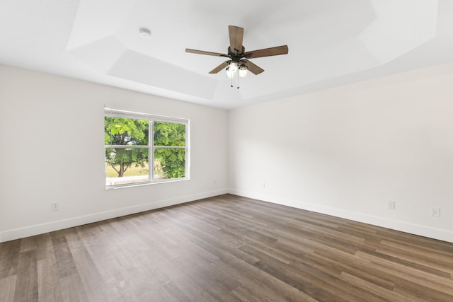 unfurnished room with a raised ceiling, ceiling fan, and dark wood-type flooring