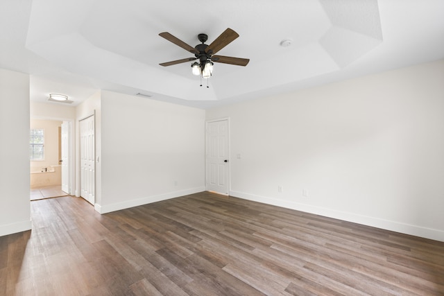 spare room with dark hardwood / wood-style flooring, a raised ceiling, and ceiling fan