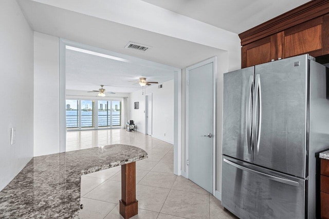 kitchen featuring ceiling fan, stainless steel fridge, light tile patterned floors, and dark stone counters