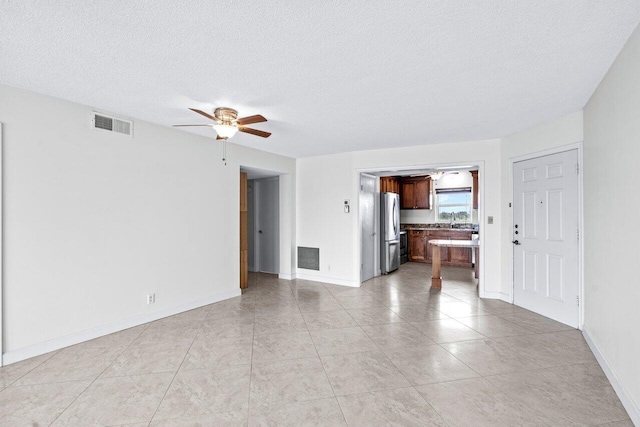 unfurnished living room featuring light tile patterned flooring, a textured ceiling, ceiling fan, and sink