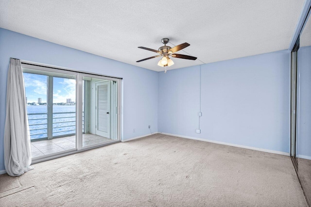 carpeted empty room featuring ceiling fan, a water view, and a textured ceiling