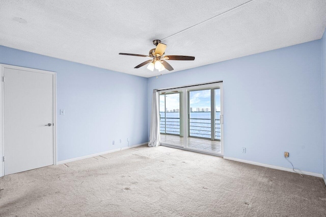 carpeted empty room with a textured ceiling, a water view, and ceiling fan