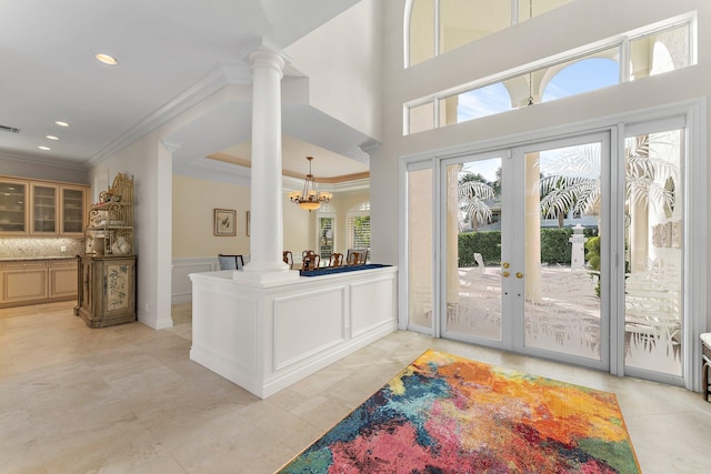 entrance foyer featuring ornate columns, french doors, a high ceiling, a notable chandelier, and ornamental molding