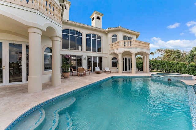 rear view of house with a swimming pool with hot tub, a balcony, and a patio