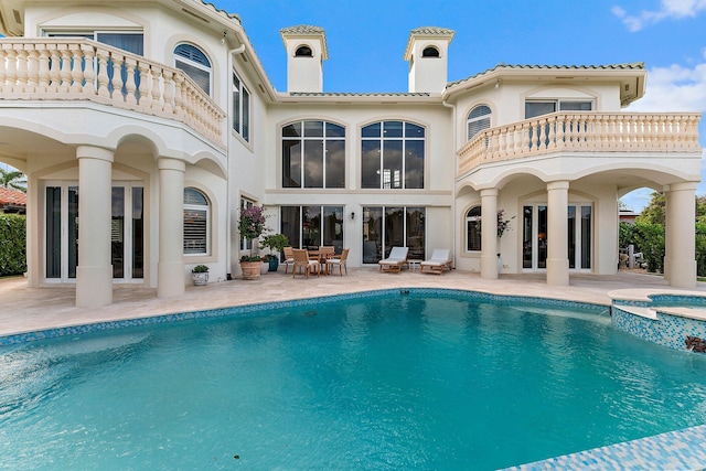 rear view of property with a swimming pool with hot tub, a patio, and a balcony